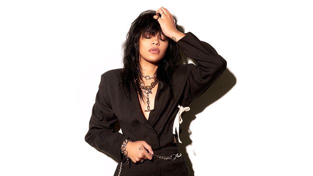 Fefe Dobson in a black outfit scrunching her hair against a white backdrop.