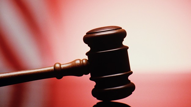 GAVEL RESTING ON REFLECTIVE BENCH SURFACE WITH AMERICAN FLAG IN BACKGROUND