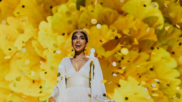 Rupi Kaur standing in front of a yellow flower