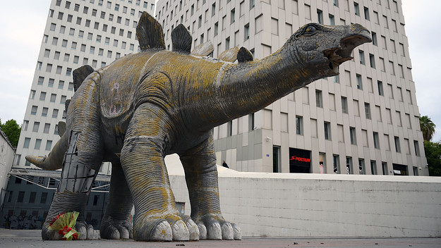 Flowers are placed near a large statue of a dinosaur in Santa Coloma de Gramanet.