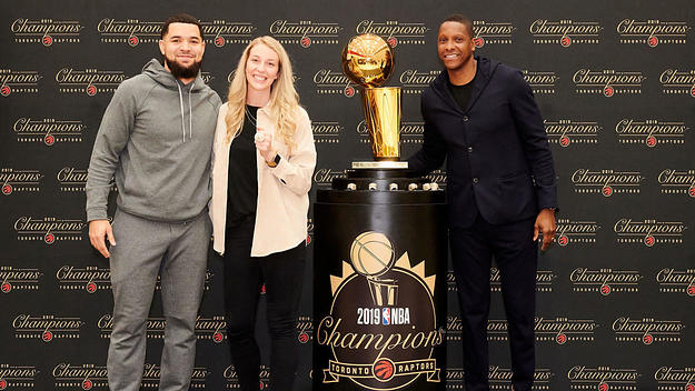 Toronto Raptors' Shelby Weaver poses with Fred VanVleet, Masai Ujiri, and the Larry O'Brien trophy