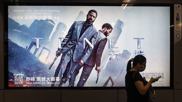 A commuter walks past a poster of Christopher Nolan's blockbuster film Tenet