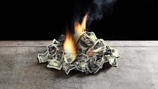 Pile of 100 dollar notes on table on fire.