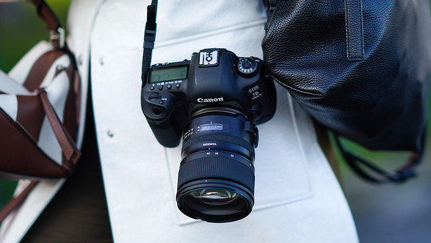 A guest wears a black bag, a white trench coat, a Canon EOS 5D Mark IV DSLR camera.