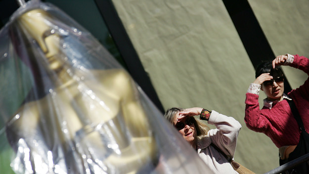 Two women stand next to an Oscar as they watch the Oscar Statues parade