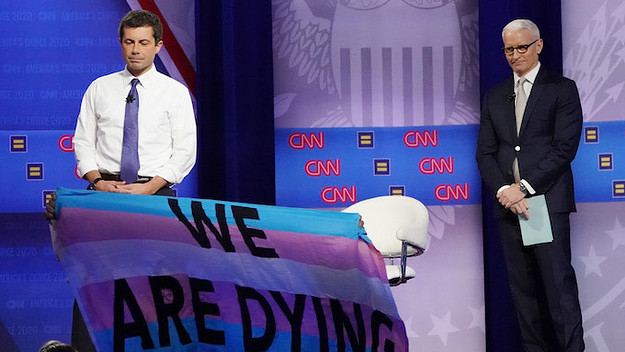 Pete Buttigieg and Anderson Cooper react as protestors display banners.