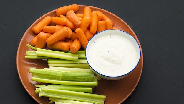 Baby carrots, celery sticks and a bowl full of delicious ranch sauce placed in a brown plate.