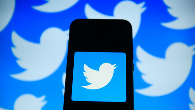 Twitter logo is seen on an android mobile phone in front of a computer screen