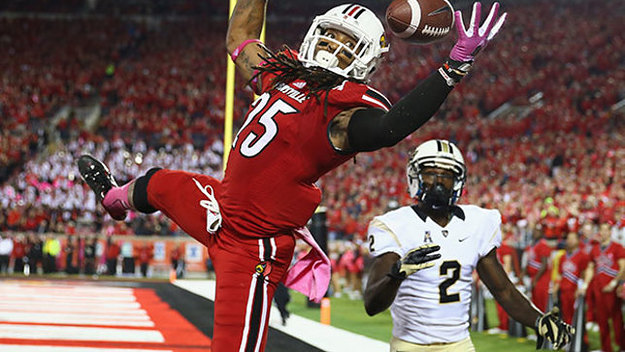 A football player in a red uniform leaps to catch a pass in the end zone, with an opposing player in white nearby.