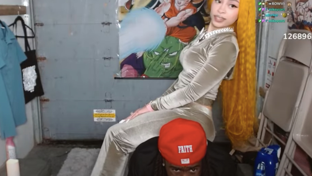Kai Cenat and Ice Spice posing in a themed room; Ice Spice in a velvet outfit, and Kai Cenat in a red cap