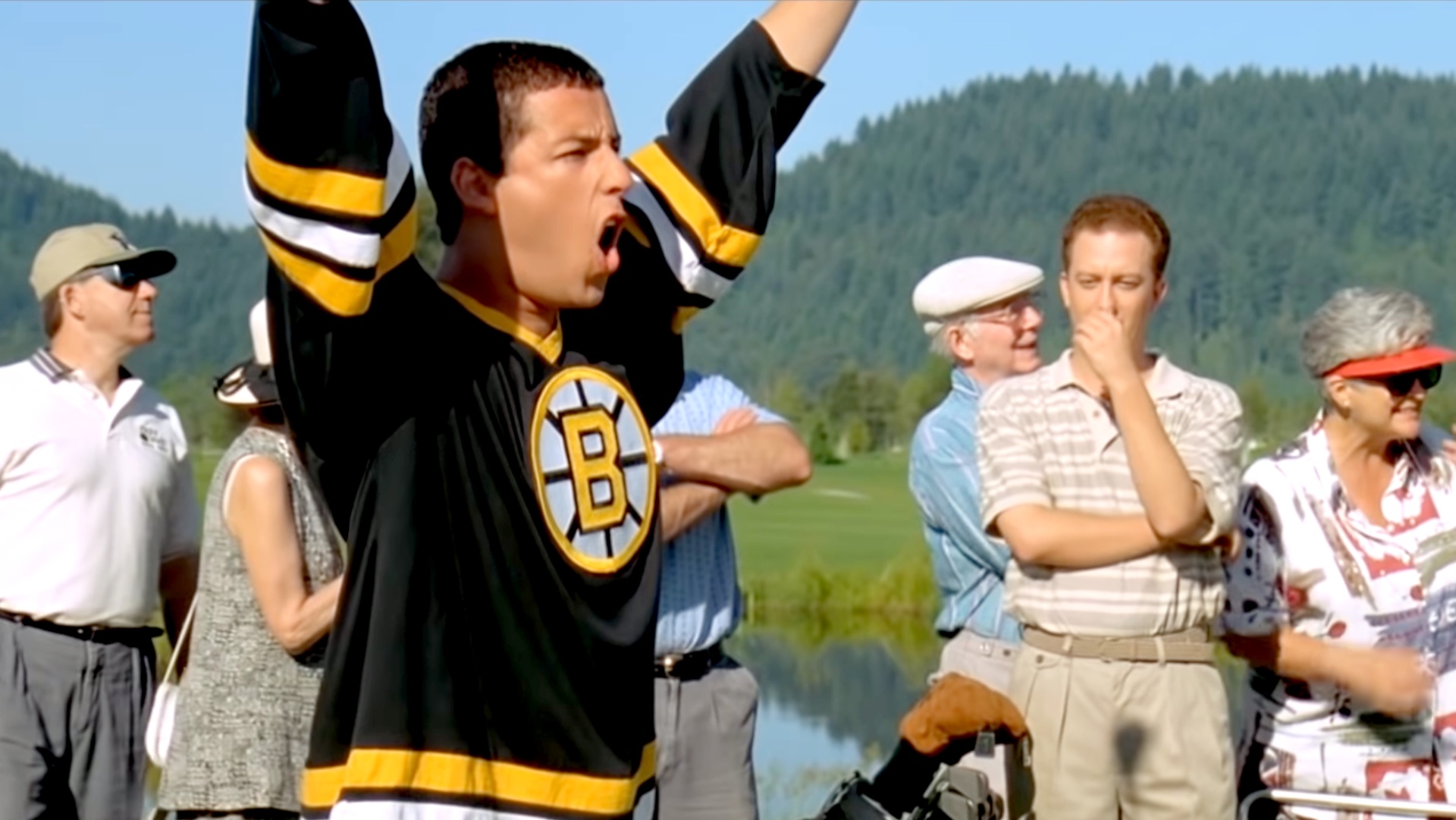 Happy Gilmore (Adam Sandler, center left) stands with his arms extended to the air as onlookers applaud and cringe.