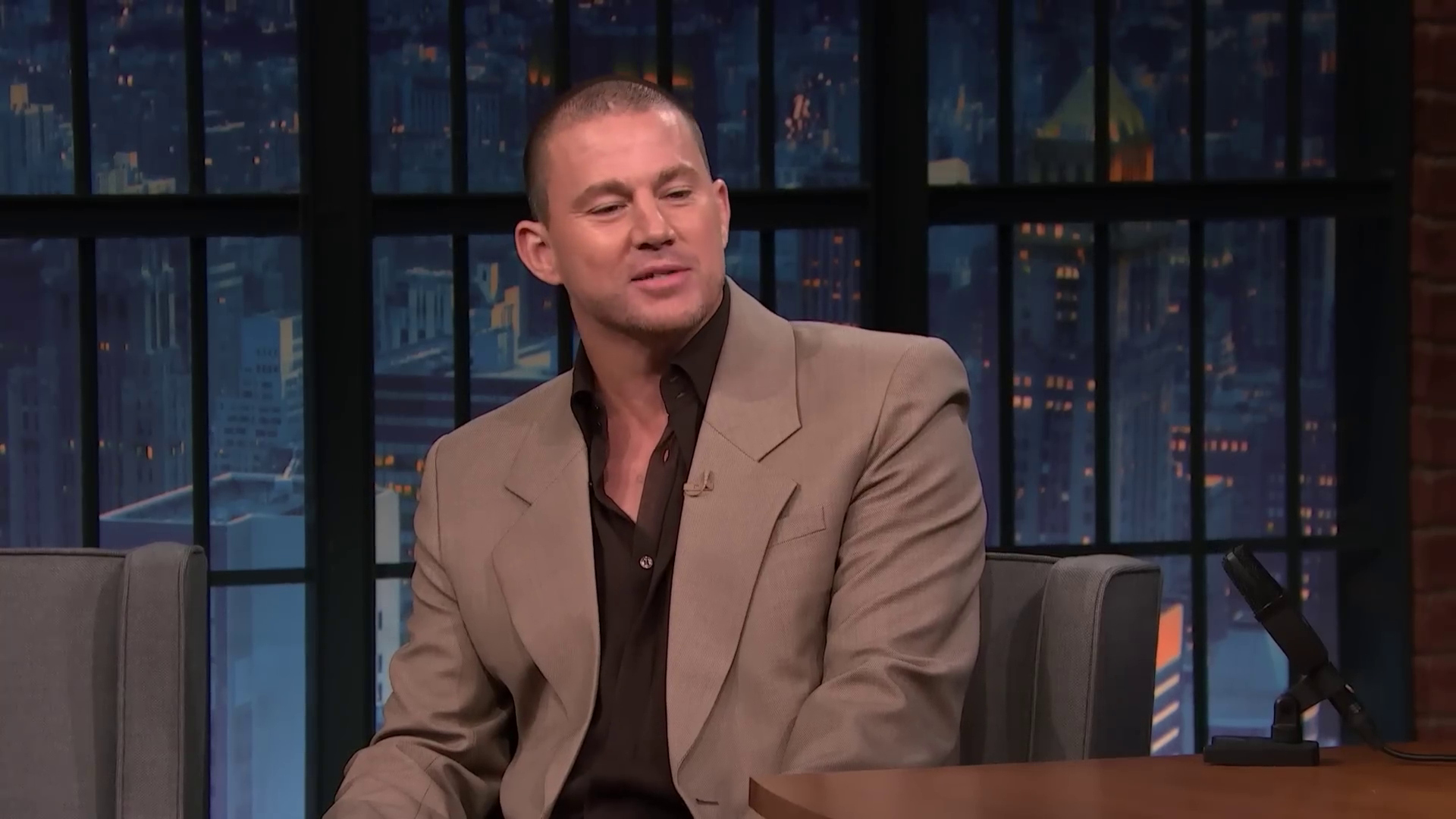 Channing Tatum in a tan suit sitting in a TV studio set