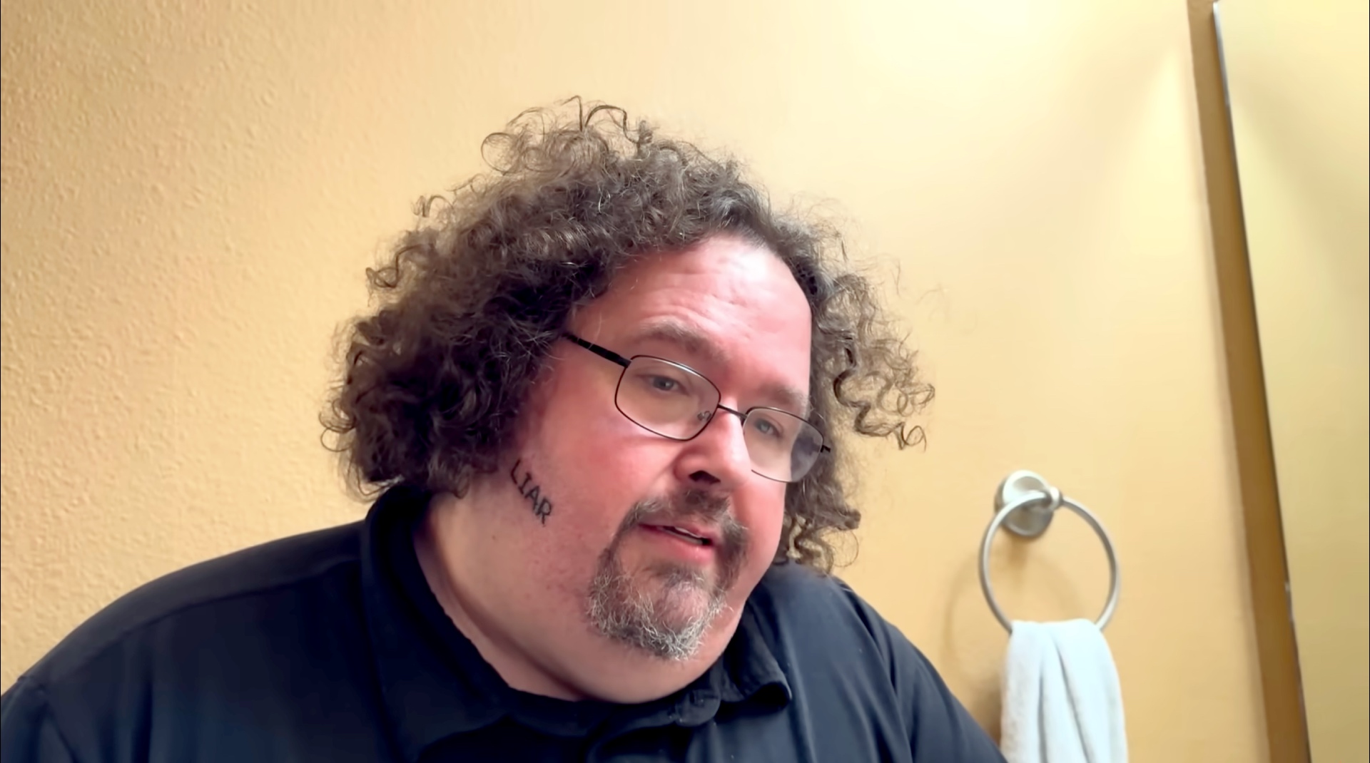 Steven "Boogie2988" Williams stands in a bathroom talking about the "Liar" tattoo he has on his right cheek.