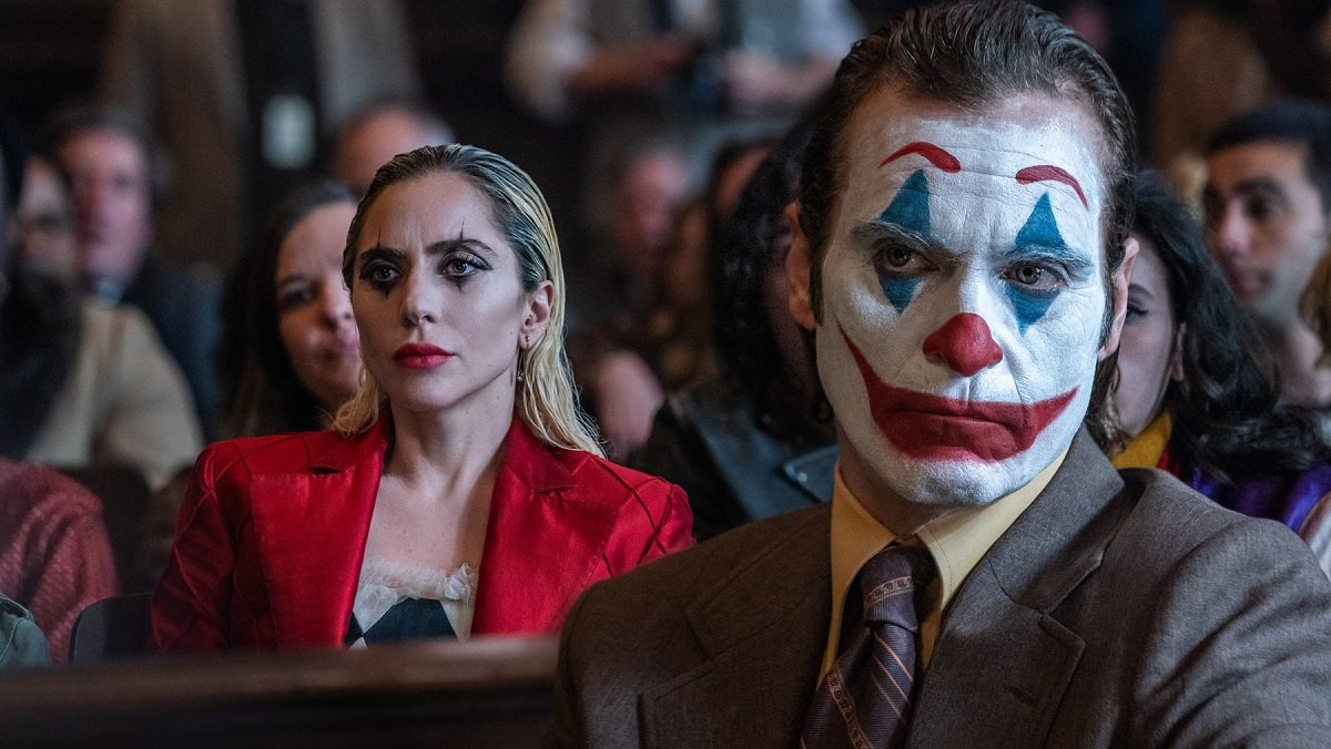 Harley Quinn (Lady Gaga, left) and The Joker (Joaquin Phoenix, right) sit in a courtroom surrounded by people.