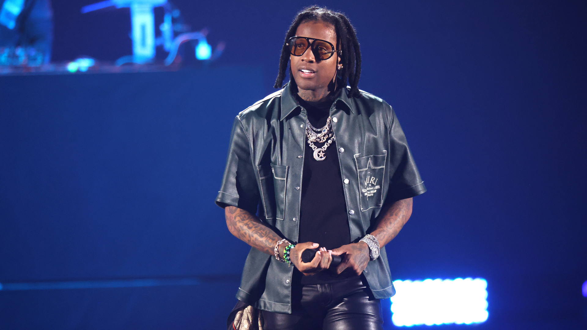 Lil Durk performs on stage, wearing a dark shirt and leather pants.