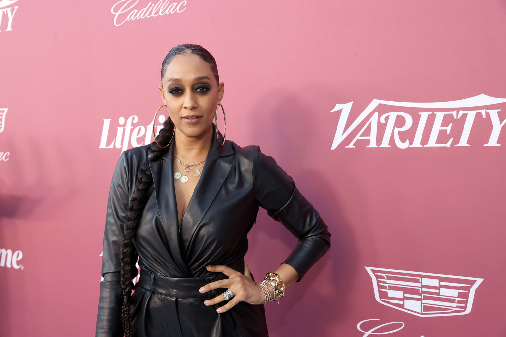 Tia Mowry poses in a black leather outfit at a Variety event, with a pink background featuring logos like Cadillac and Lifetime.