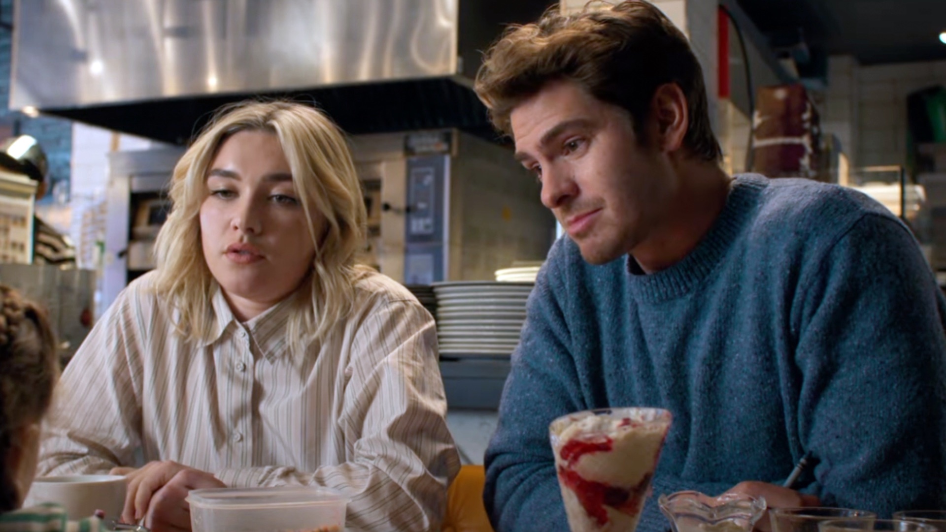 Almut Brühl (Florence Pugh, left) and Tobias Durand (Andrew Garfield, right) sit inside what appears to be a diner with food in front of them.