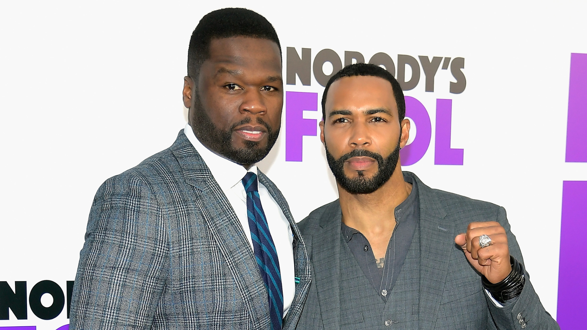 50 Cent and Omari Hardwick at the "Nobody's Fool" premiere, both in suits, posing together with a promotional background.