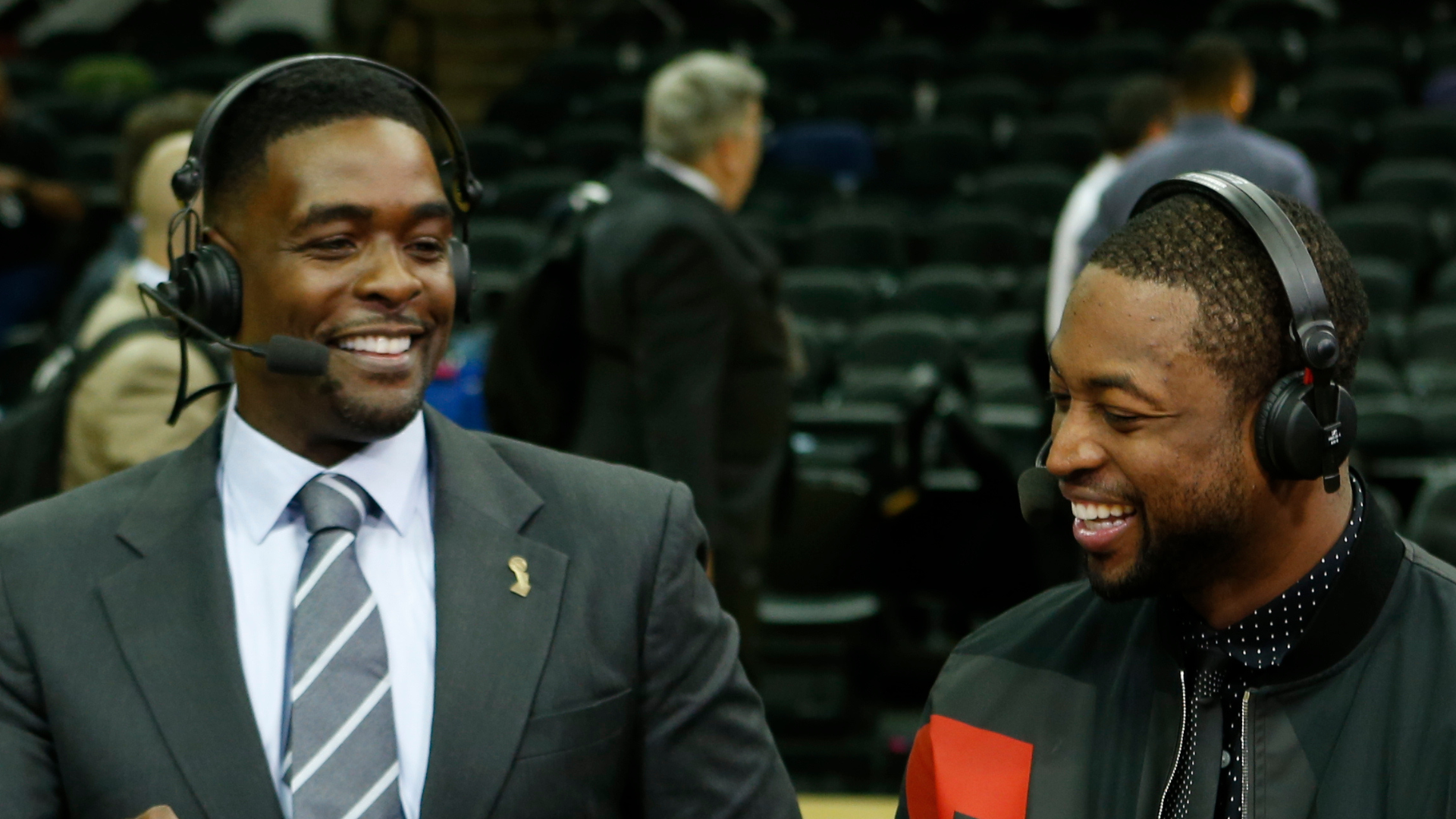 Chris Webber and Dwyane Wade are smiling, wearing headsets, and engaging in conversation at a sports event.