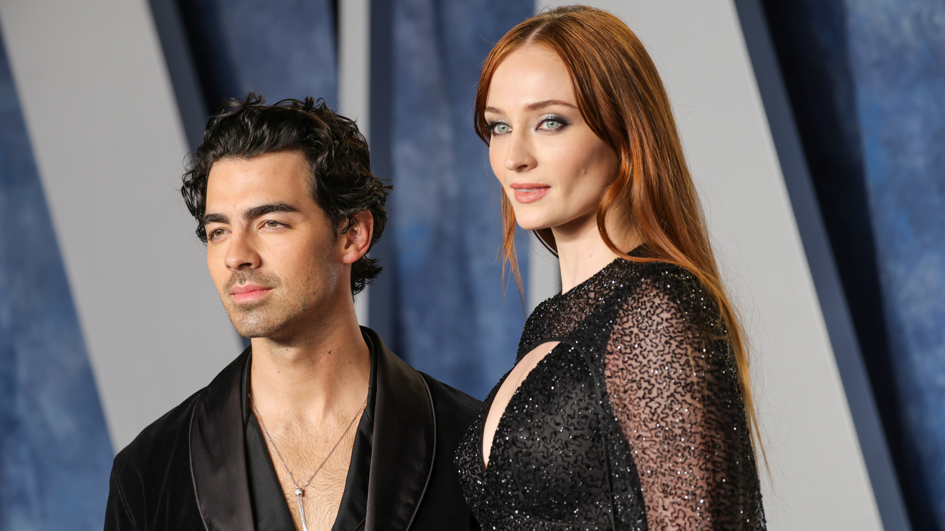 Joe Jonas and Sophie Turner pose together at an event. Joe wears a dark suit, and Sophie wears a sparkling black dress.