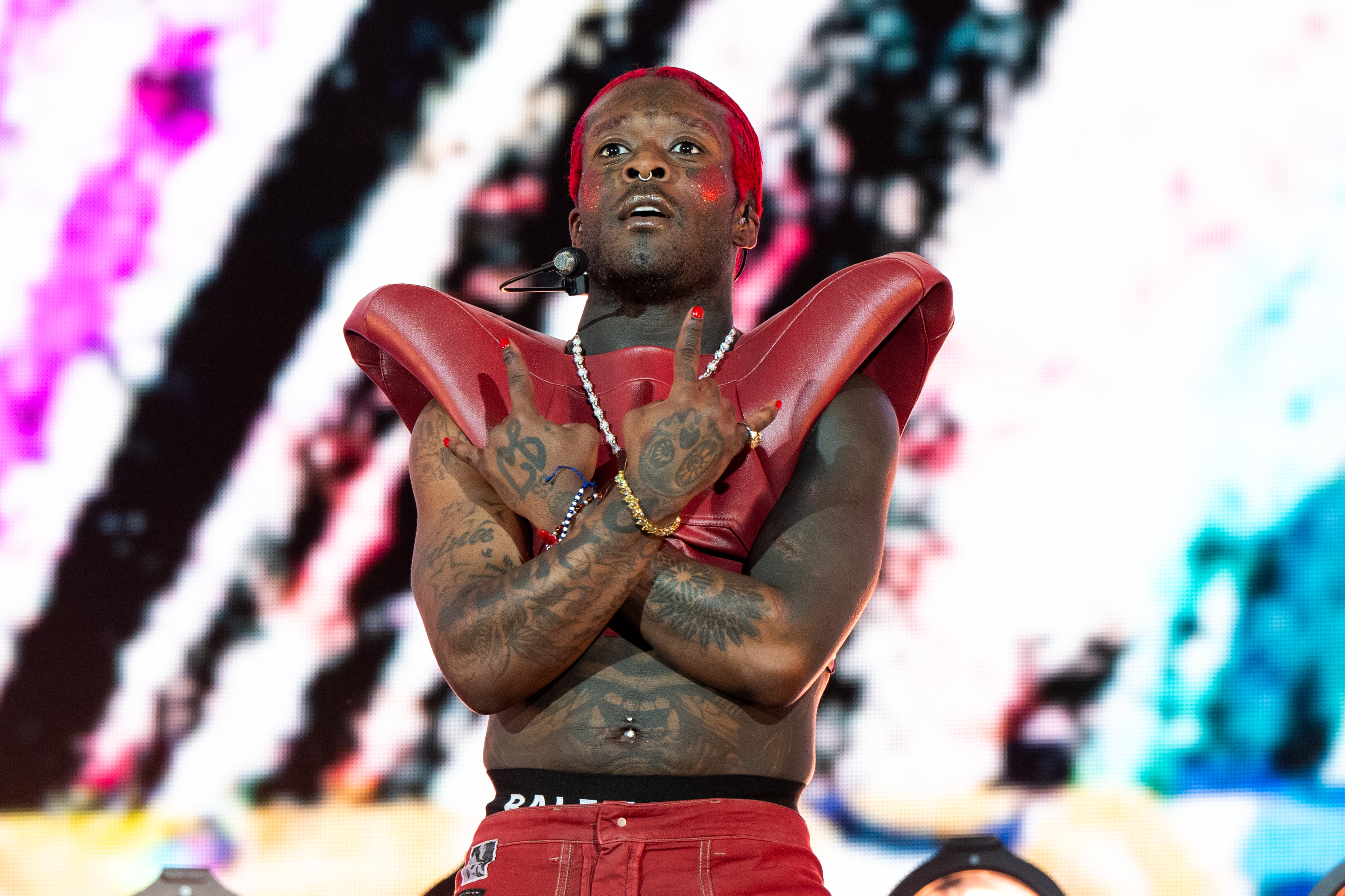 Lil Uzi Vert performing on stage, wearing red attire and shoulder pads, with colorful background visuals.