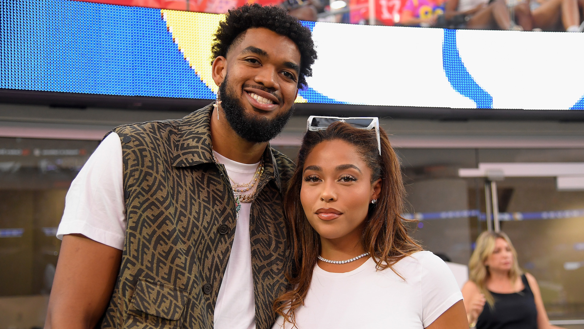Karl-Anthony Towns and Jordyn Woods smiling together at an event, with a colorful background.