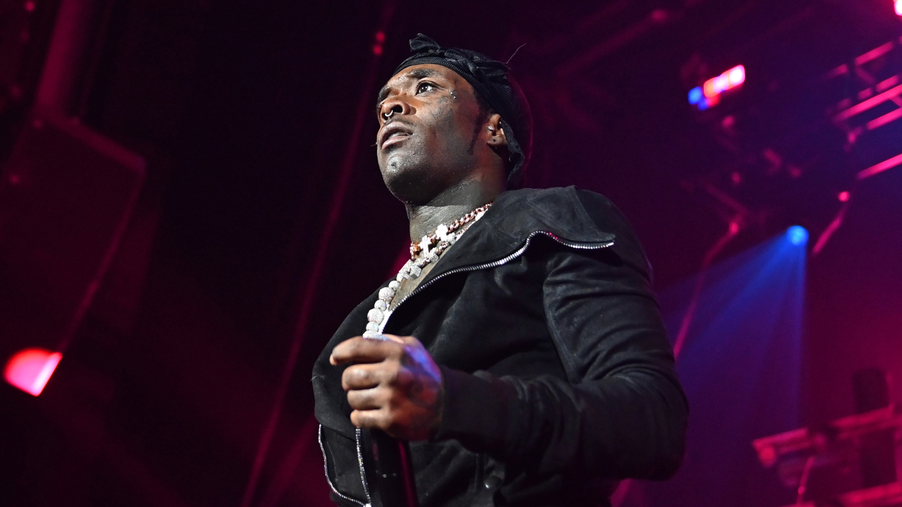 Lil Uzi Vert performing on stage, wearing a black outfit and holding a microphone, with vibrant stage lighting in the background.