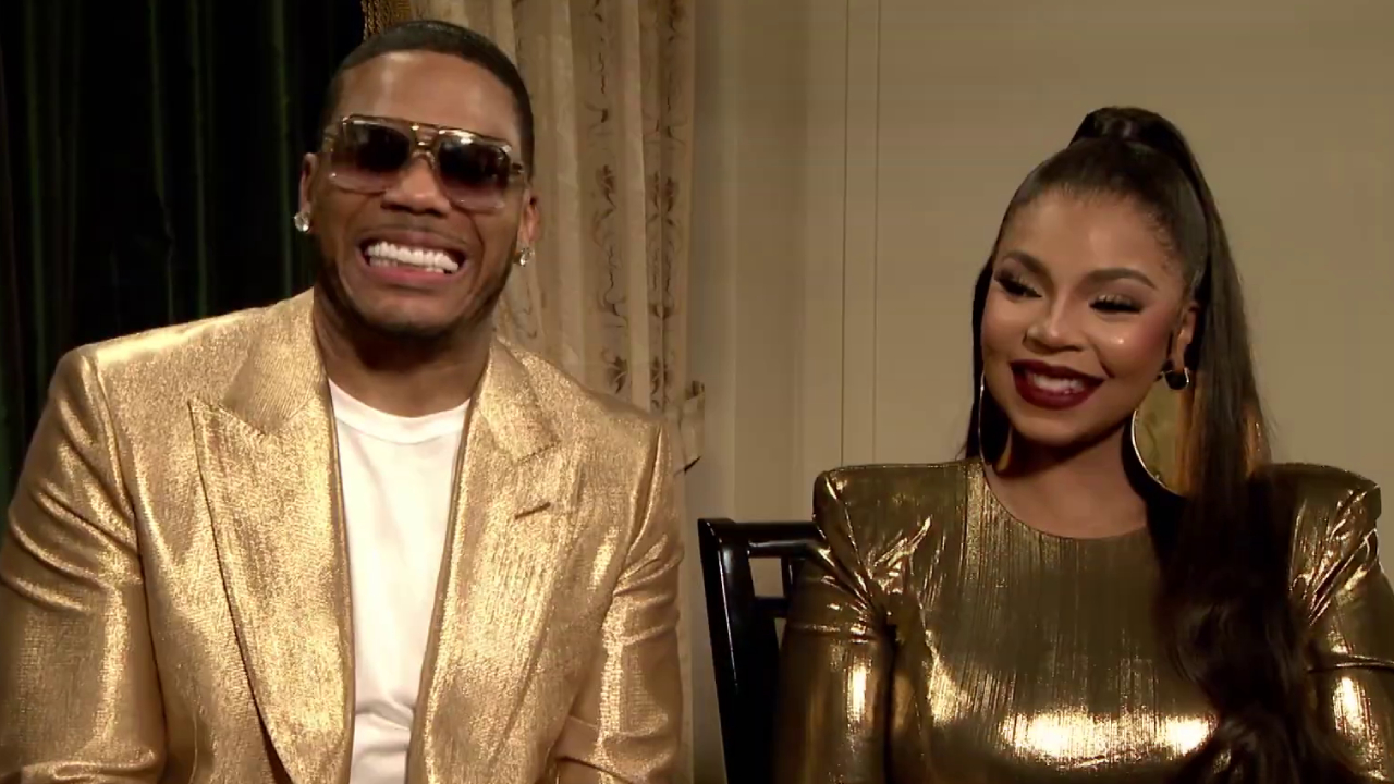 Nelly and Ashanti smiling together, both wearing matching gold outfits. Nelly is in sunglasses, Ashanti has long hair styled up.
