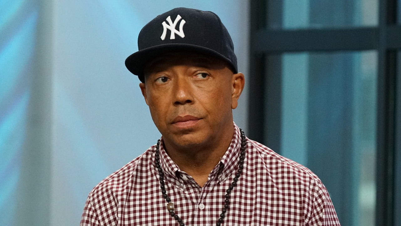 Russell Simmons wearing a New York Yankees cap and a checkered shirt, looking thoughtful.
