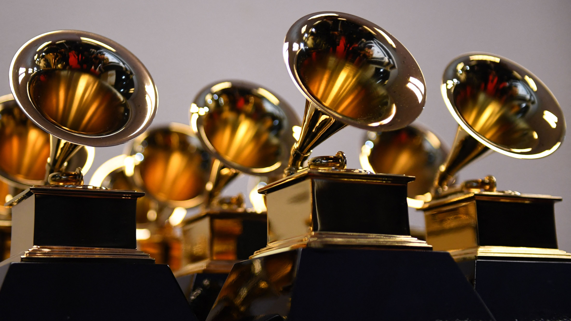 A collection of shiny Grammy Award trophies with golden gramophones on black bases, arranged closely together.