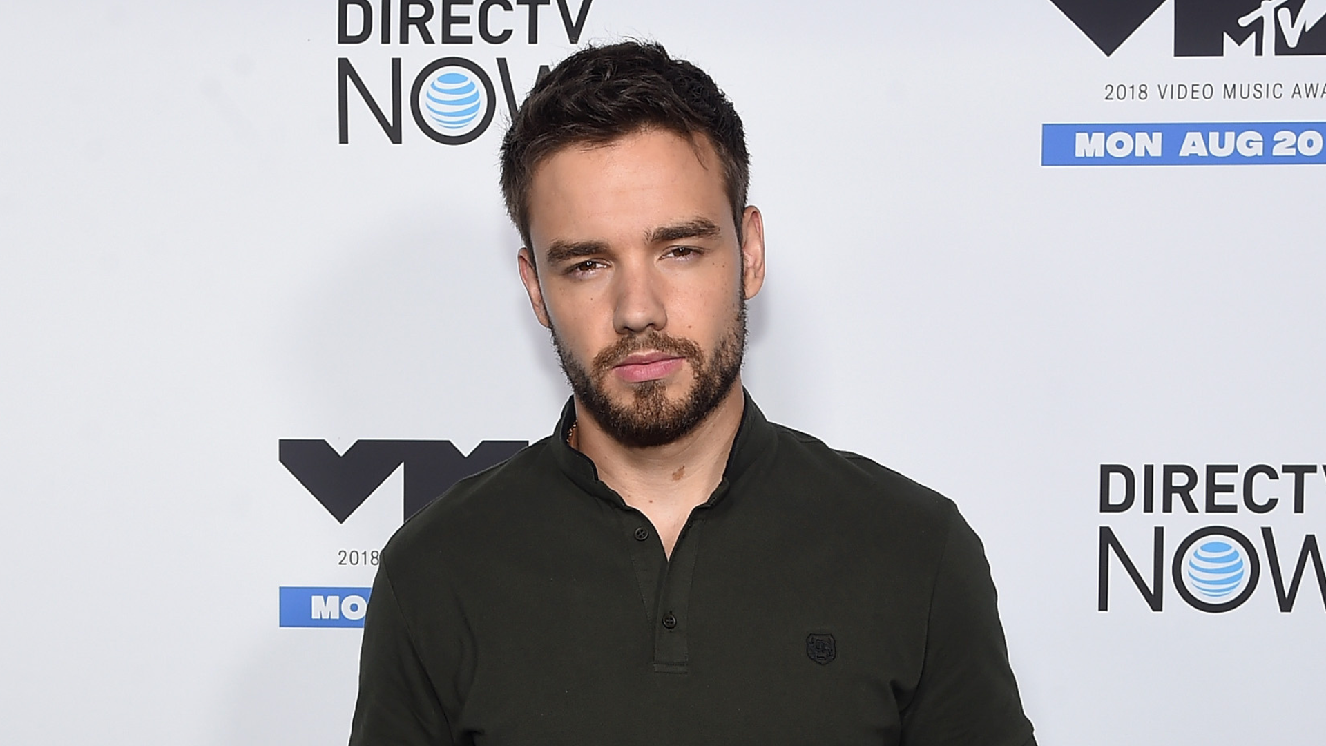 Liam Payne at the 2018 MTV Video Music Awards, wearing a dark green shirt, standing in front of a media wall with event logos.