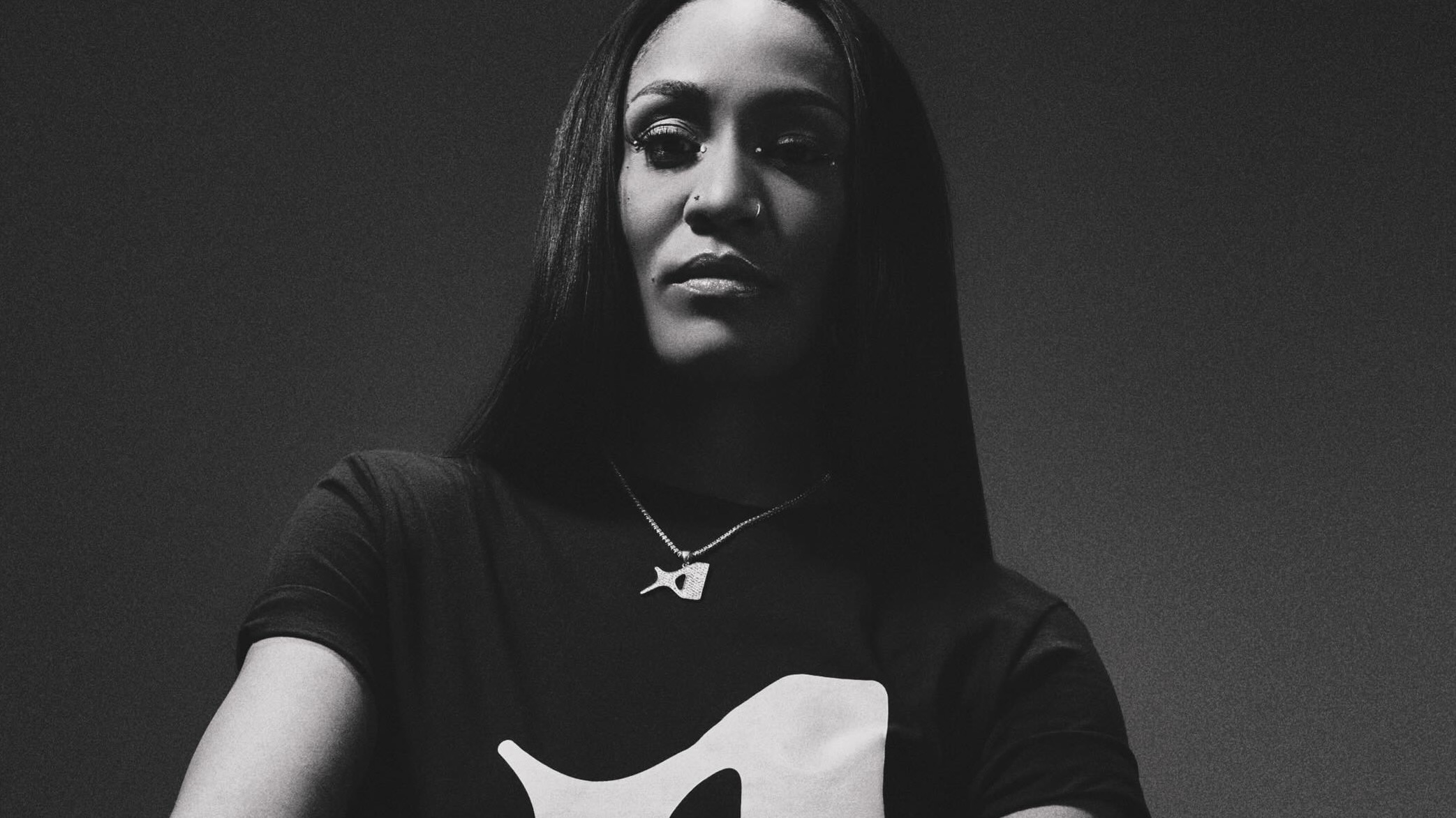 A woman with long hair wearing a t-shirt and necklace, posed confidently in a black and white image. A'ja Wilson nike wnba