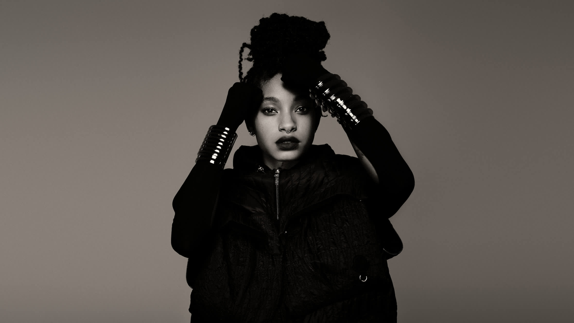 Willow in a black outfit poses with her hands on her head. The image is in black and white.