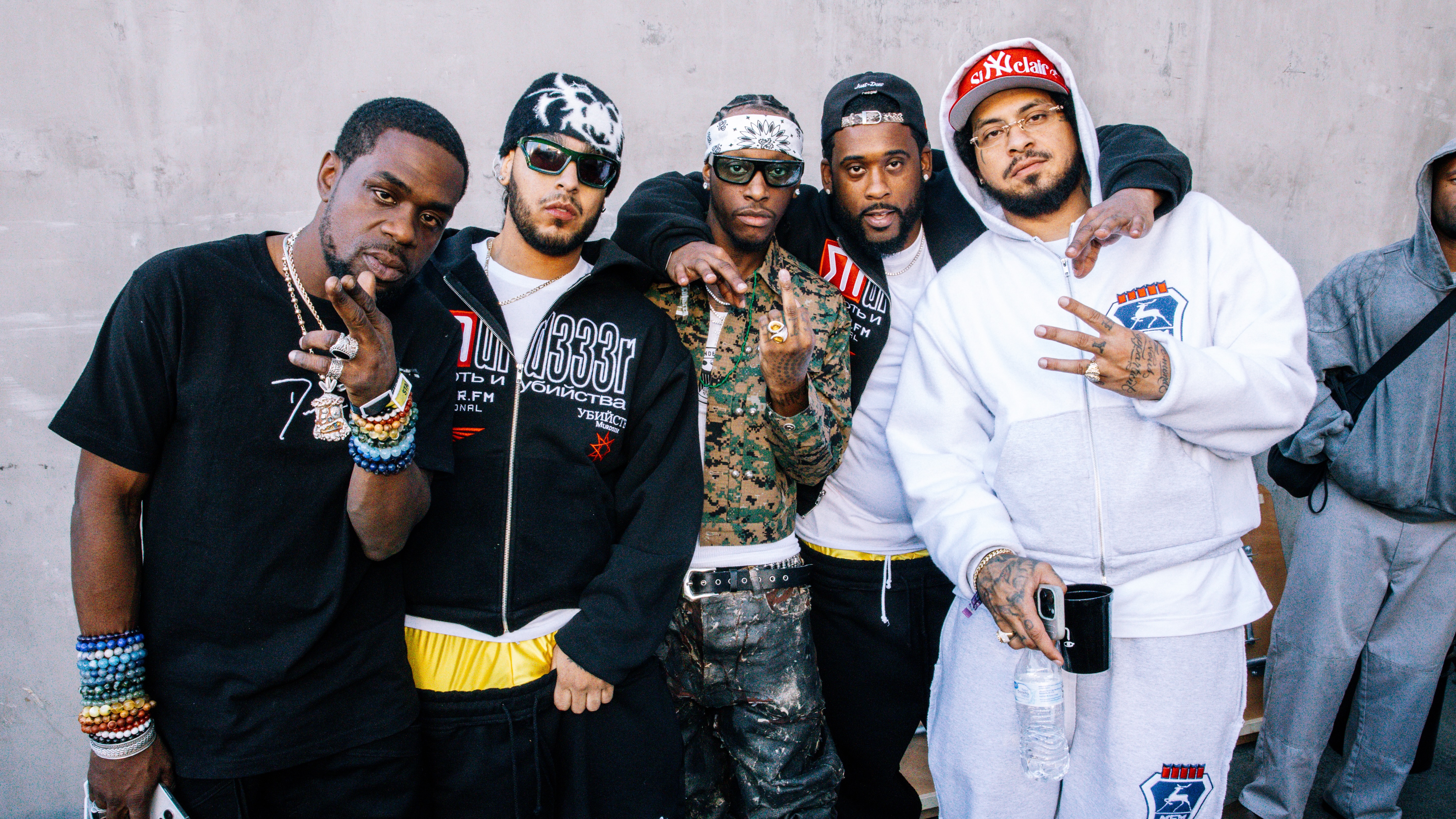 A group of five men posing together, wearing casual streetwear and accessories, standing against a concrete wall. complexcon Las Vegas 2024 bloody Osiris