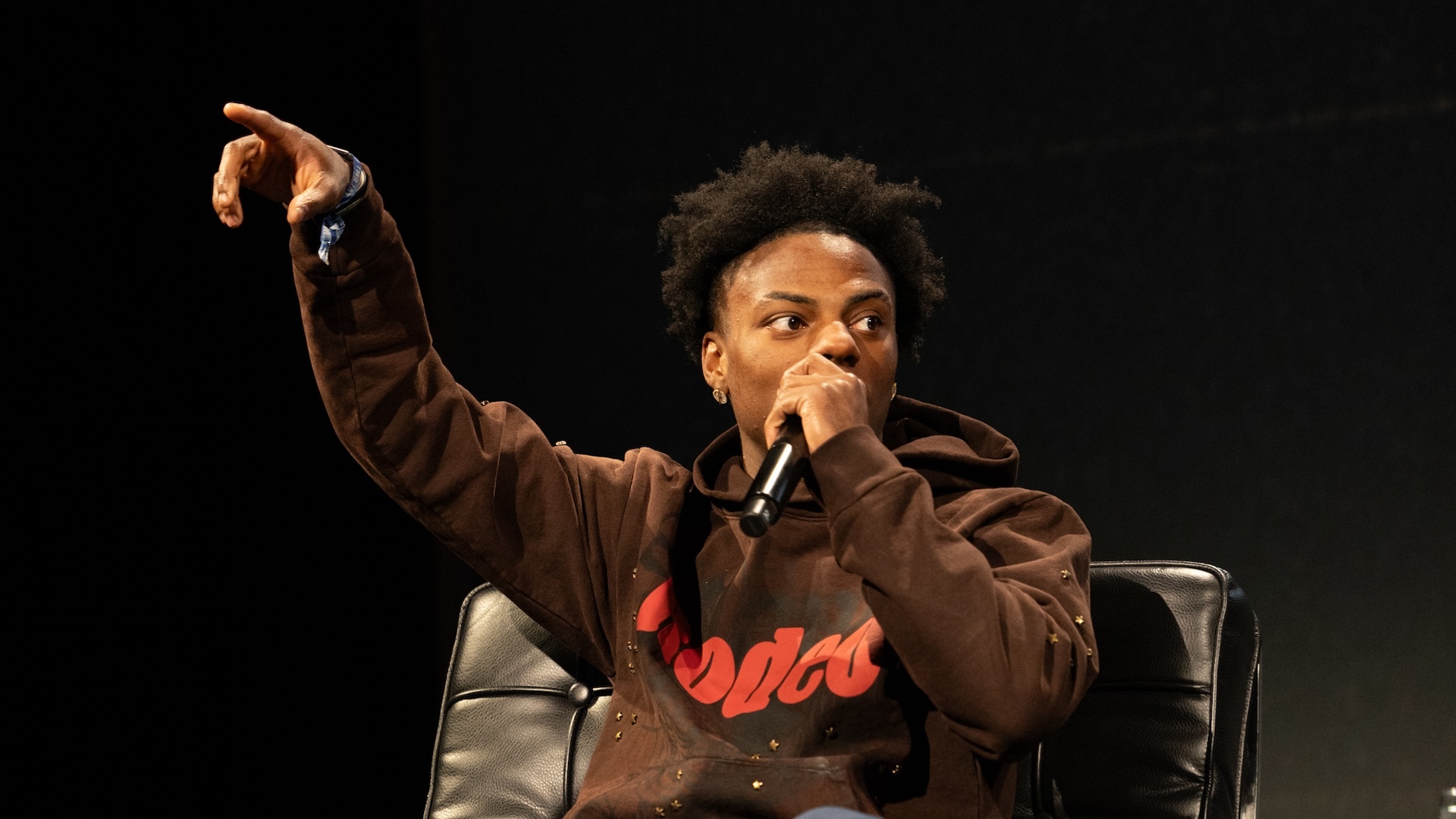 iShowSpeed on stage at ComplexCon 2024 wearing a brown hoodie and holding a microphone.