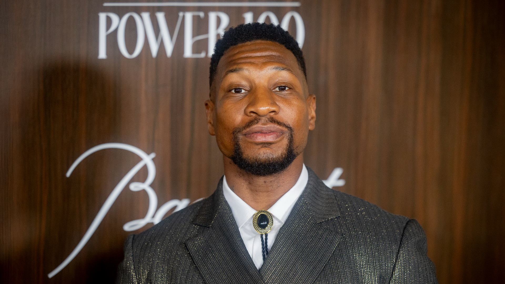 A man in a suit stands in front of a wooden backdrop with "Power 100" written on it.