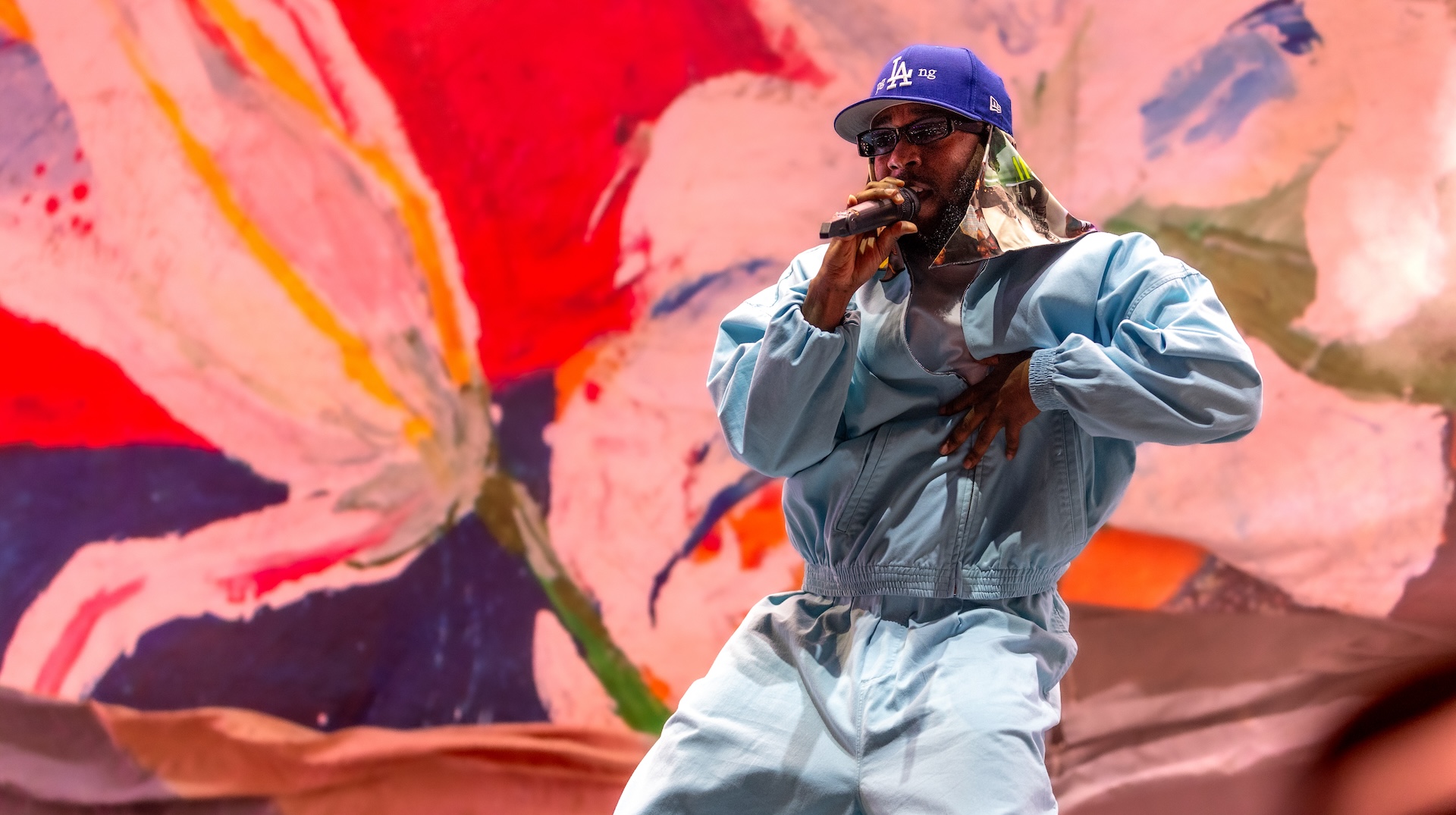 Kendrick Lamar sings into a microphone on stage with a colorful abstract background.