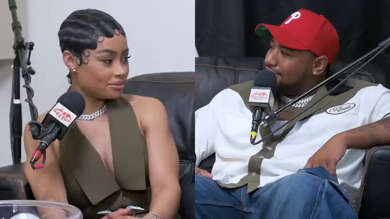 Angela White (formerly known as Blac Chyna) and fiancé Derrick Milano are sitting and talking into microphones during a podcast. He wears a red cap, and she has a stylish short hairstyle.