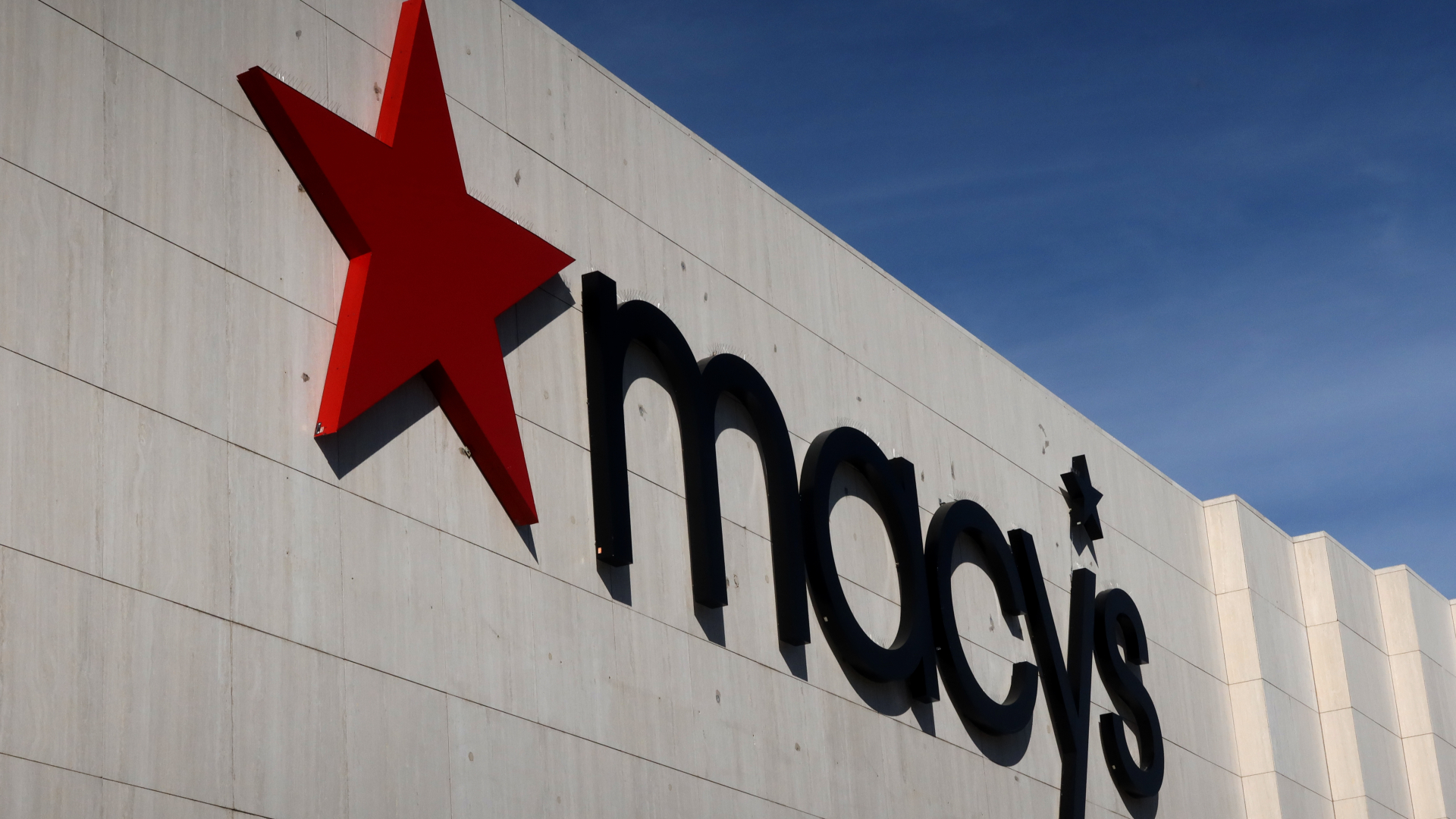 The image shows the Macy's logo on a building, featuring a large red star and the name "macy's" in black letters.