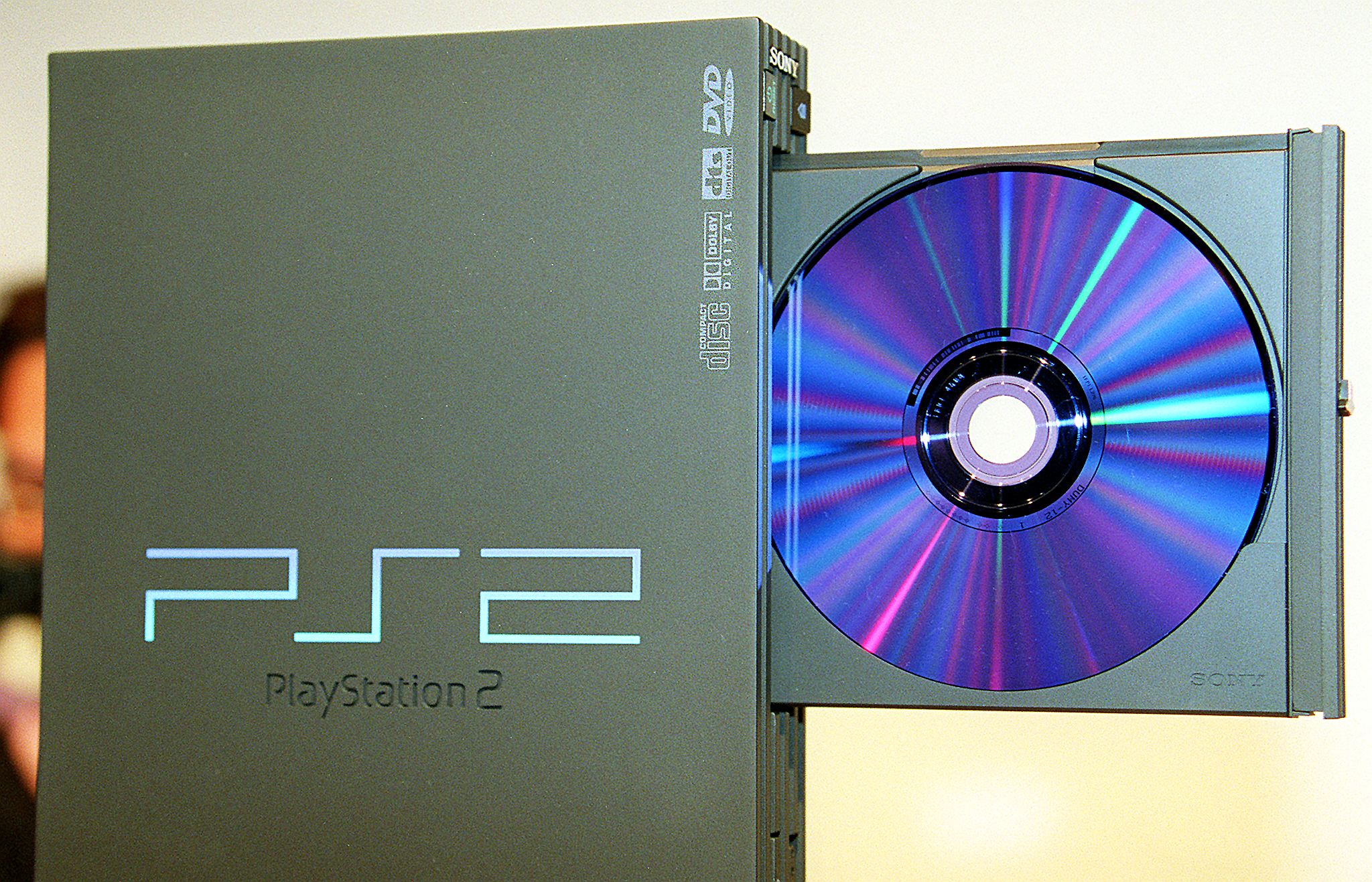 A PlayStation 2 console with an open disc tray showing a blue disc.