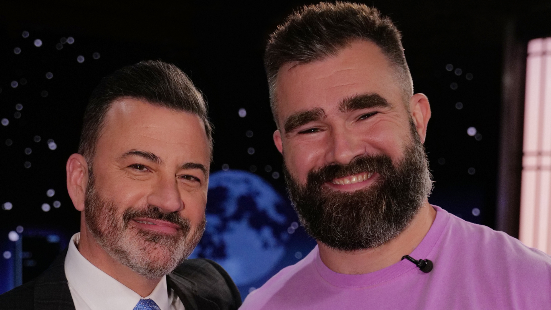 (L) Jimmy Kimmel in a suit and tie (R) Jason Kelce with a beard wearing a purple shirt.