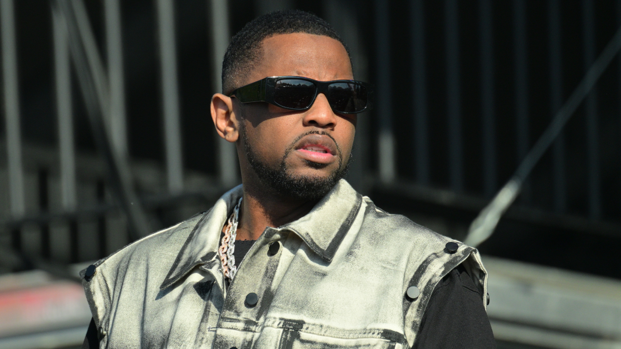 Fabolous wearing sunglasses and a denim vest, looking to the side.