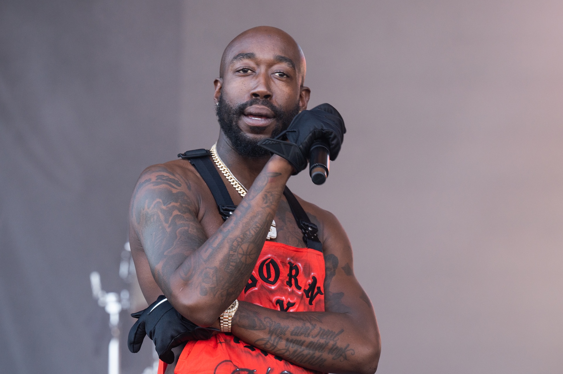 Rapper Freddie Gibbs performing on stage, wearing a red outfit and black gloves, holding a microphone.
