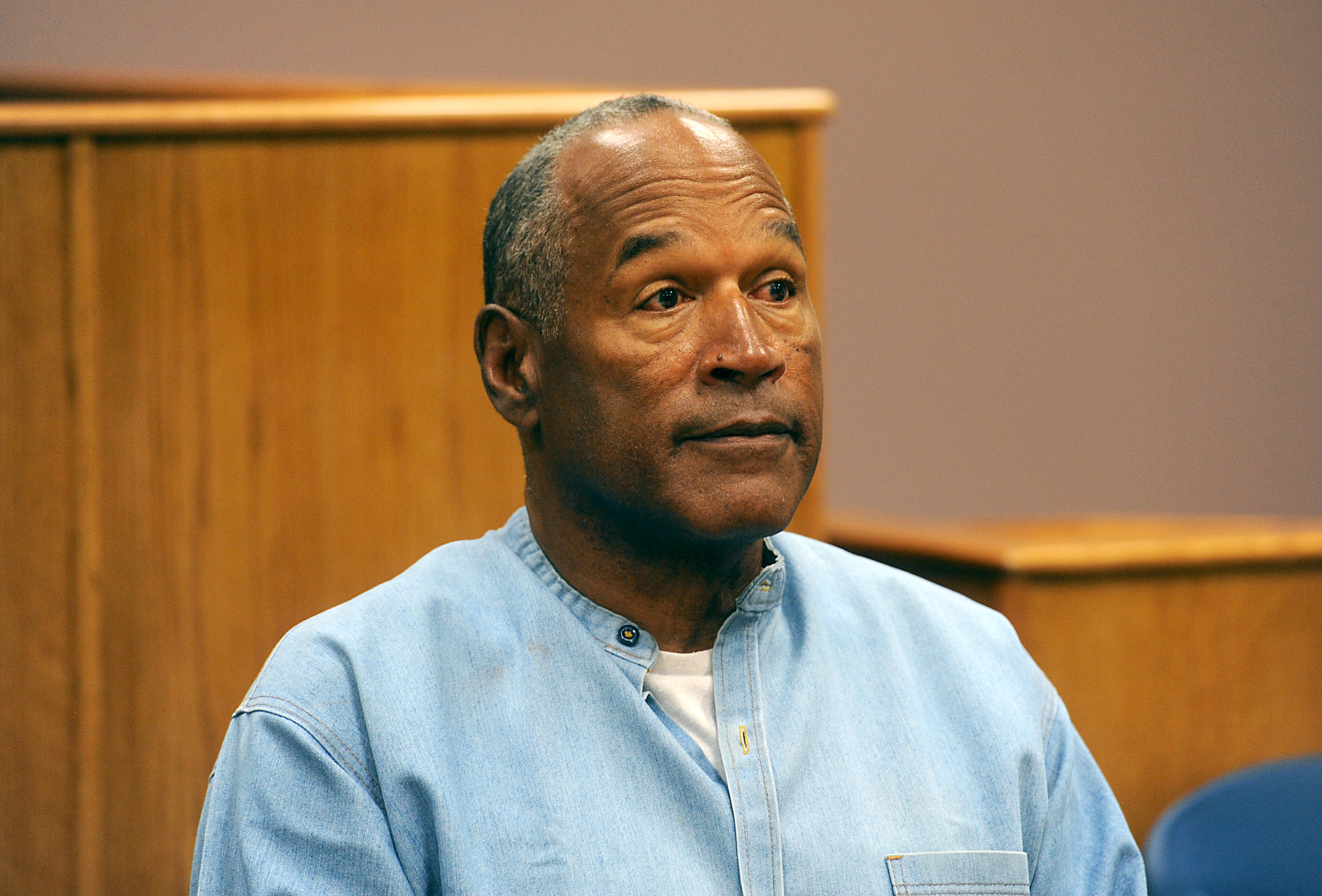 O.J. Simpson in a courtroom setting, wearing a light blue shirt, looking forward.