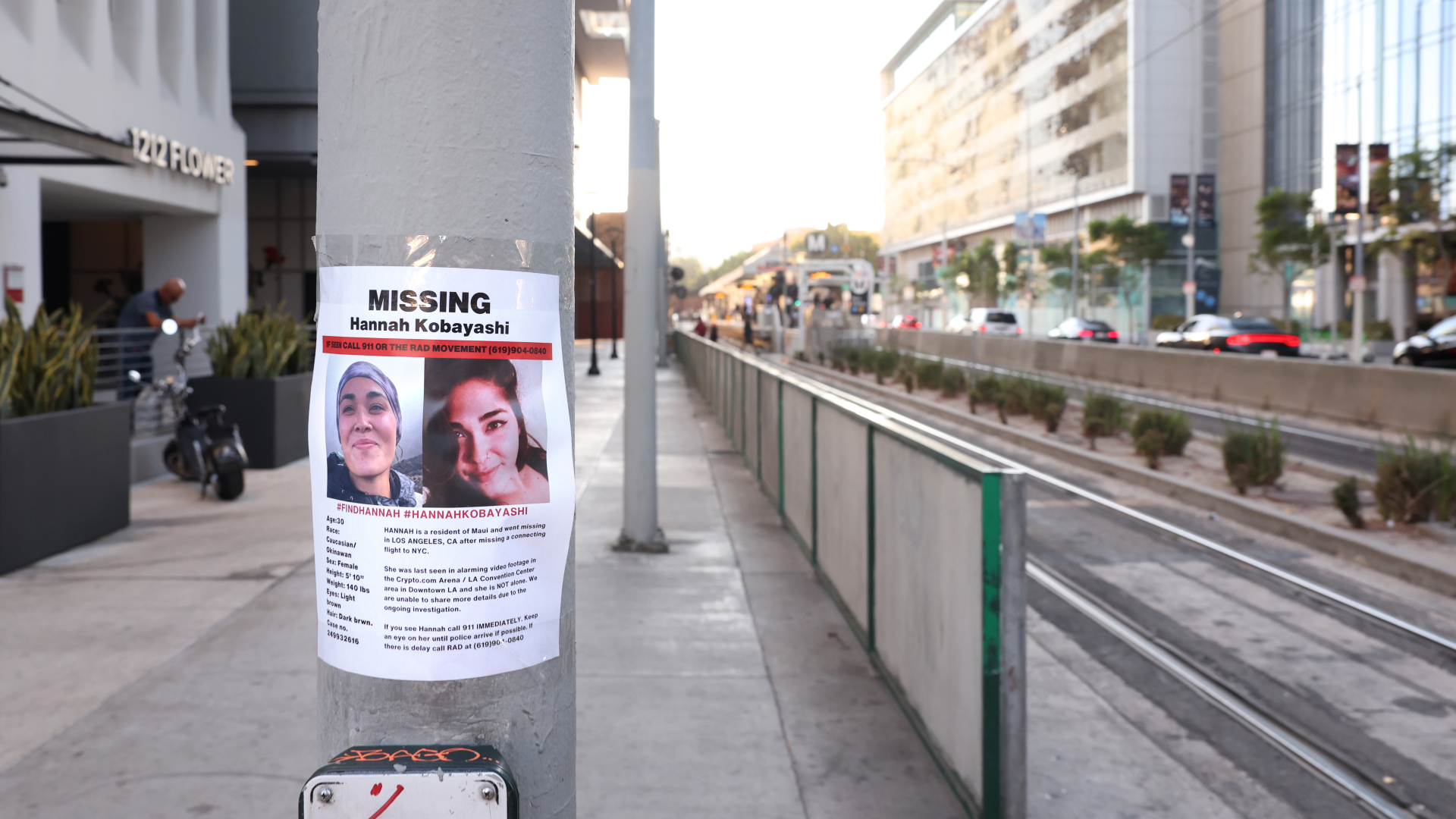 A missing person poster for "Hannah Kobayashi" is taped to a pole near a streetcar line in an urban area.