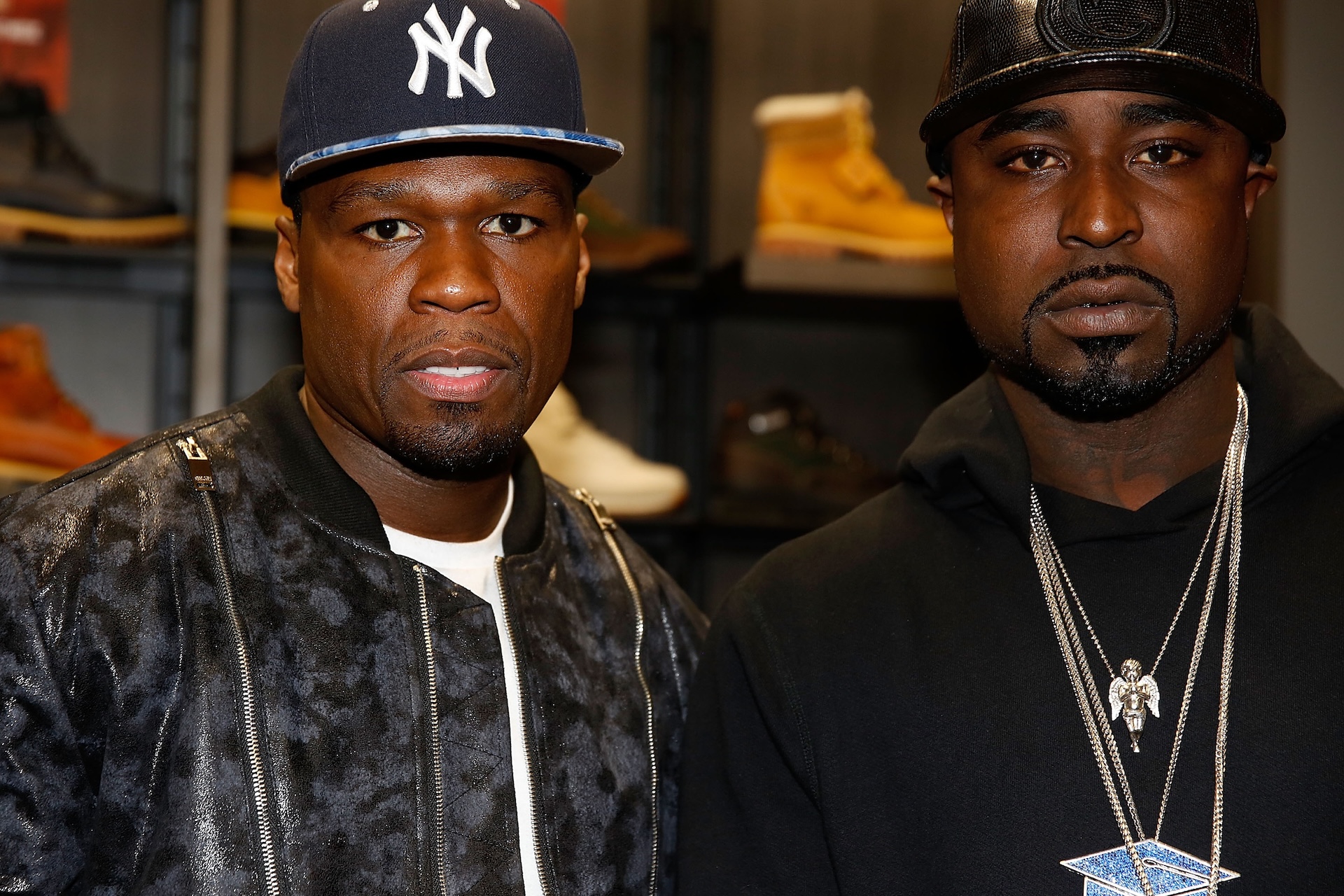50 Cent and Young Buck, both wearing caps and jackets, posing together in a store with shoes in the background.
