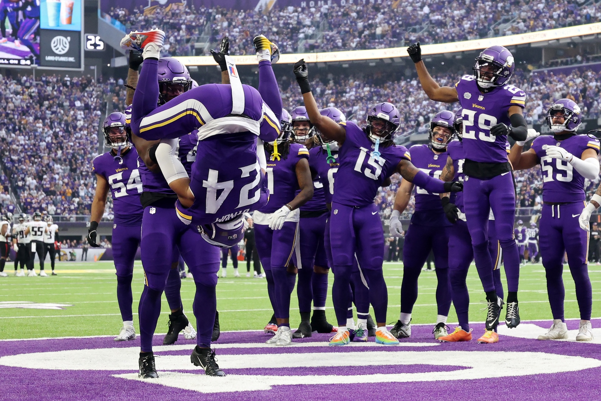 A Vikings football player wearing number 24 performs a flip in the end zone, surrounded by teammates in purple uniforms celebrating.