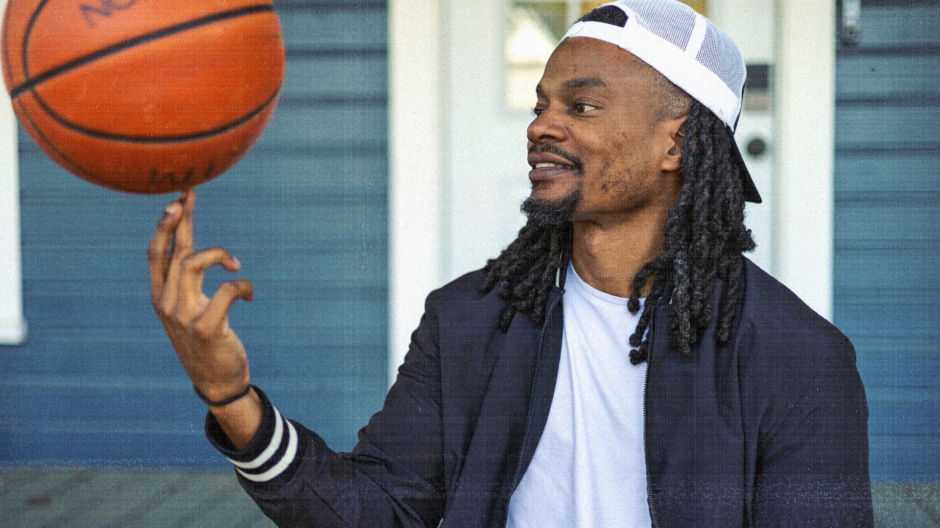 David Rushing spins a basketball on his finger, smiling, in front of a blue house.