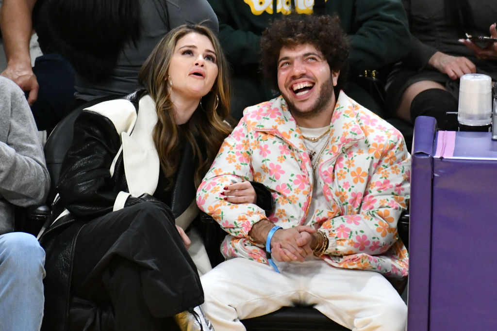 Selena Gomez and Benny Blanco sitting courtside at a basketball game, smiling and enjoying the event.