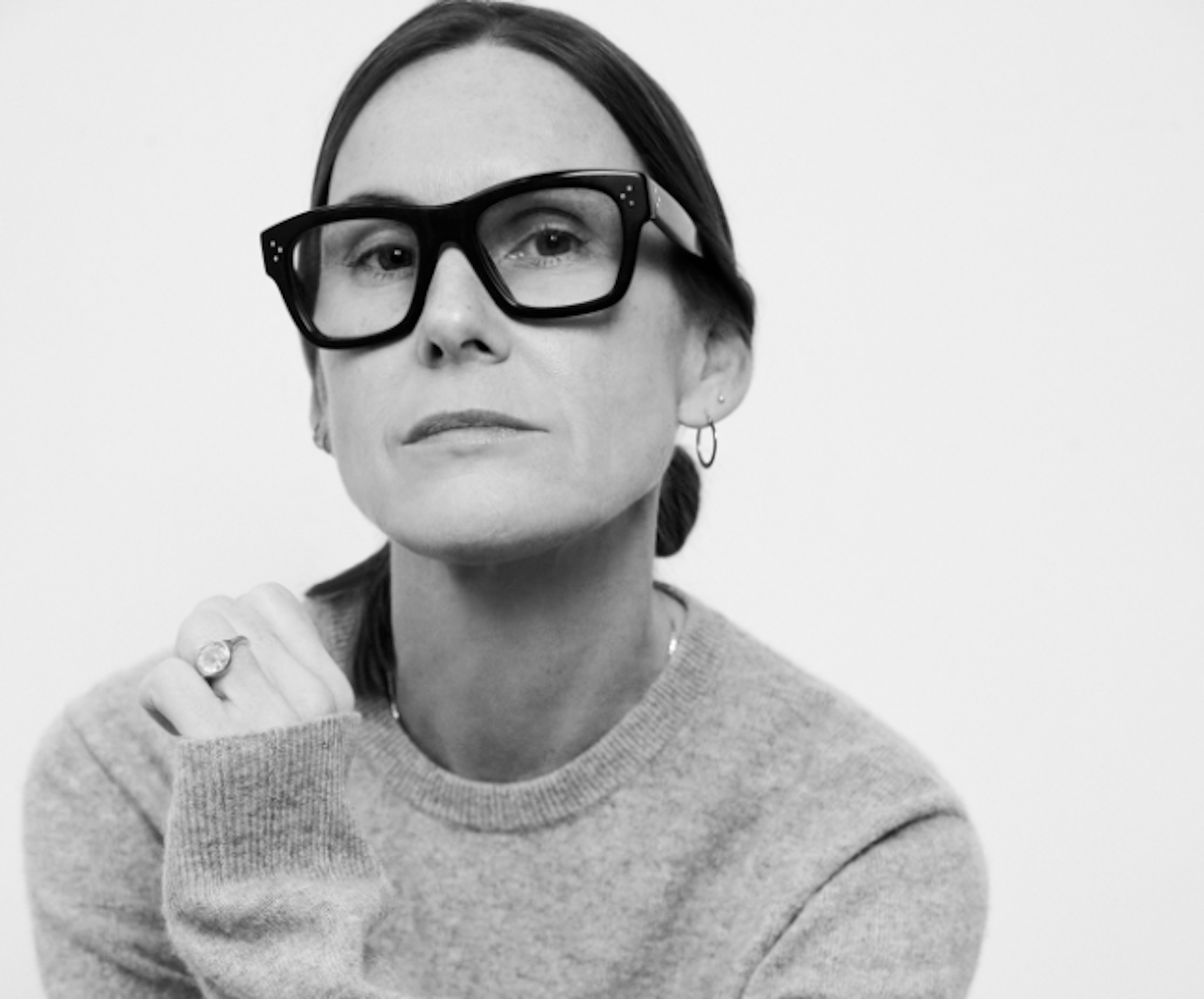 Louise Trotter wearing large black glasses and a sweater, with a thoughtful expression, resting their chin on their hand.